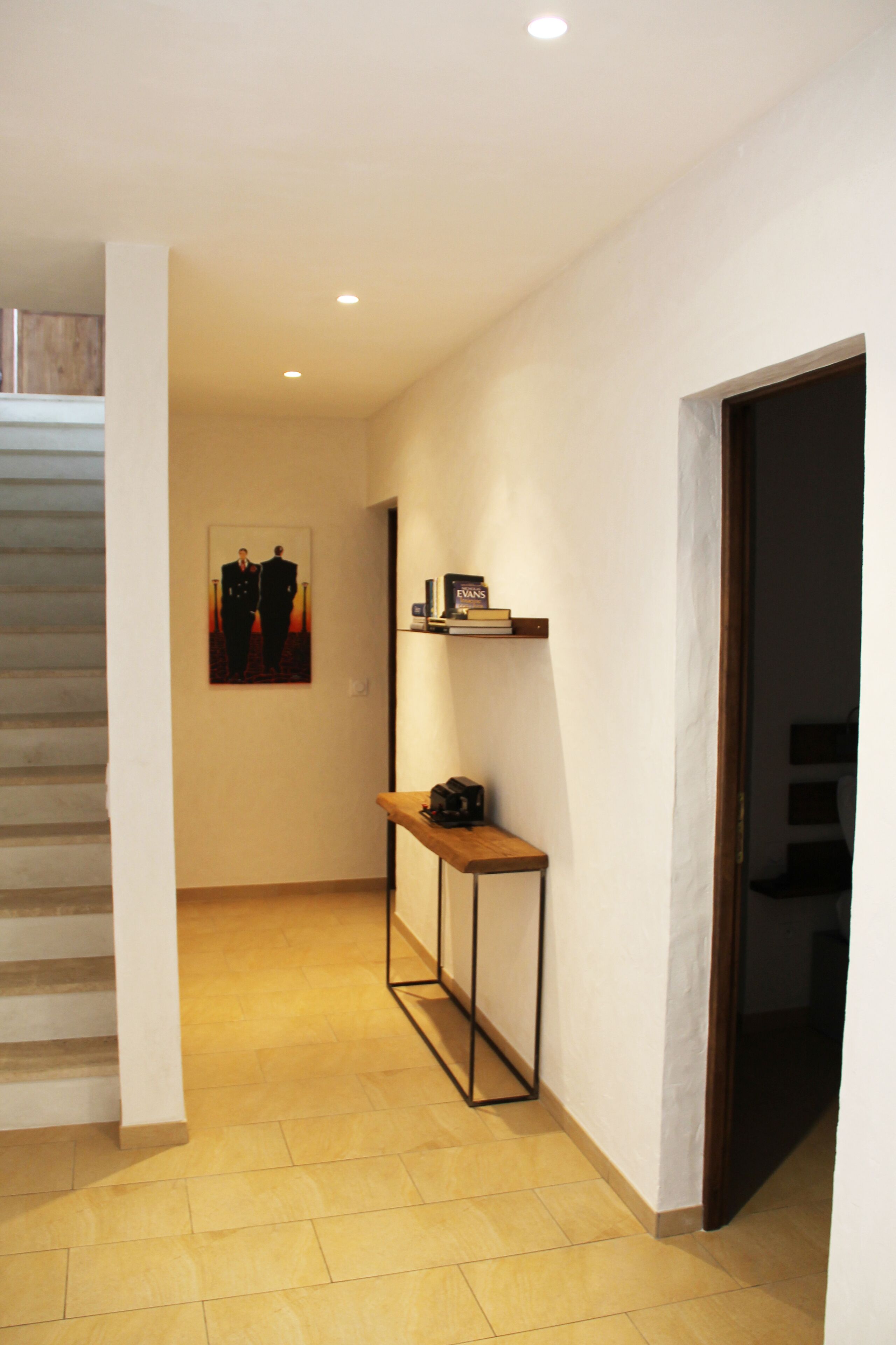 A hallway with a staircase, a small table with a telephone, and a shelf with books.