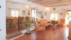 A spacious living area with a dining table, wicker chairs, a sofa, and a coffee table. There is a staircase leading to another level, and the room has tiled flooring and exposed wooden beams on the ceiling. - Villa Acuarela - 5 beds, 4 bath. Front line villa in Cala d'or. (Cala d´or)