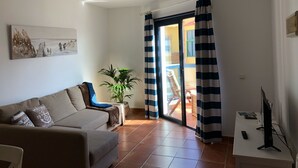 Una sala de estar con un sofá, una planta en maceta, un televisor y un ventanal corredizo que da a un área exterior.