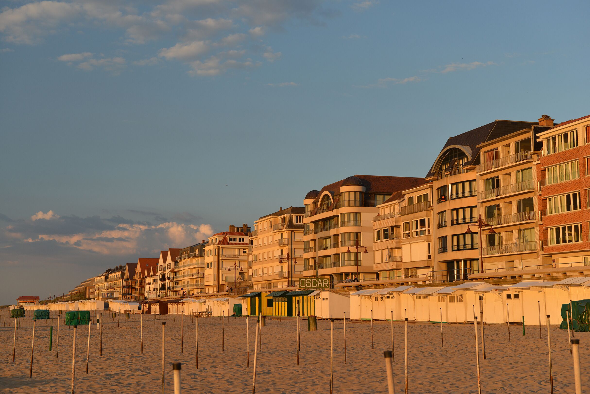 A beachfront hotel with multiple balconies, a sandy beach in the foreground, and a clear sky.