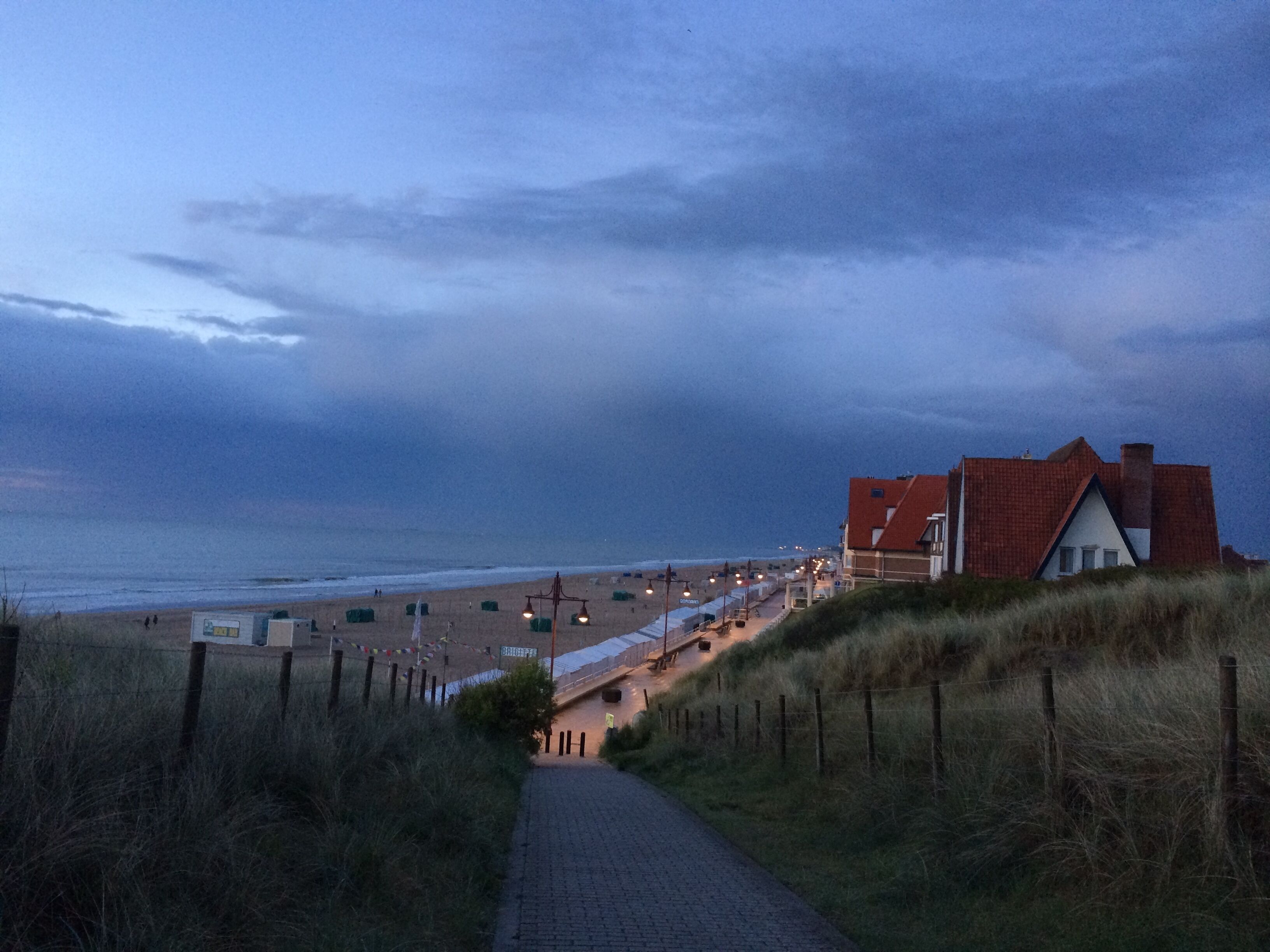 A coastal path leading to a building with a red roof, overlooking a beach.