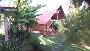 A rustic wooden structure with a corrugated metal roof, surrounded by lush greenery and a stone pathway. - Charming home comfort (LE PITON SAINT LEU)