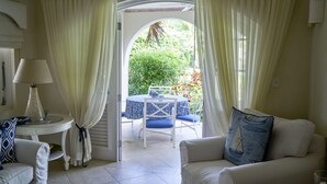 Ein Zimmer mit einer weißen Couch, einem kleinen Tisch mit Lampe und Blick auf einen Garten durch einen Bogen.