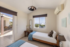 A bedroom with a bed, a bedside table, a mirror, a window with a view, and an air conditioning unit.