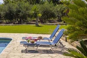 Un espace aménagé au bord de la piscine, avec des chaises longues et une table où sont servis des boissons et des en-cas.