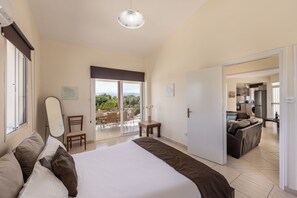 Een slaapkamer met een groot bed, een stoel, een tafel en uitzicht op de omgeving via een schuifdeur.