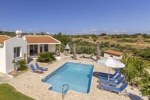 Une piscine entourée d’un jardin, avec des chaises longues et une table, et offrant une vue sur la campagne.