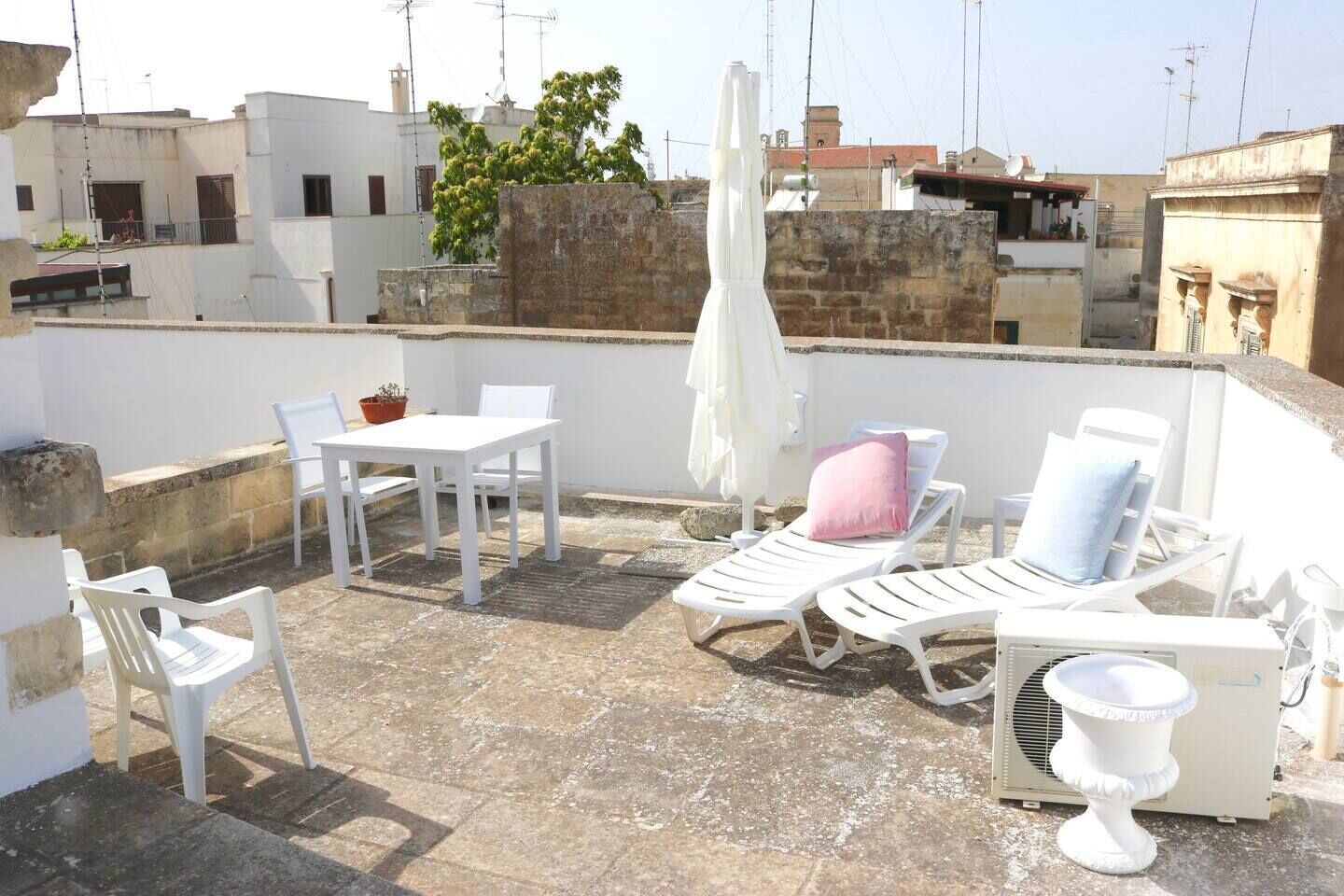 A rooftop terrace with white furniture, including a table and chairs, and lounge chairs with cushions.