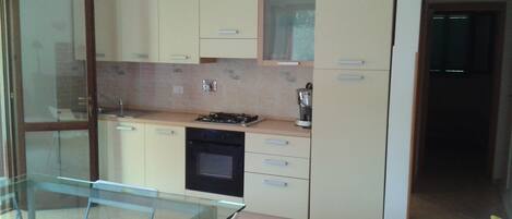 A modern kitchen with light-colored cabinets, a glass dining table, and a built-in oven.