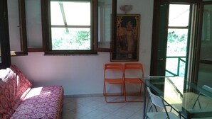 Habitació amb un sofà estampat, dues cadires taronges, una taula de vidre i un quadre a la paret.