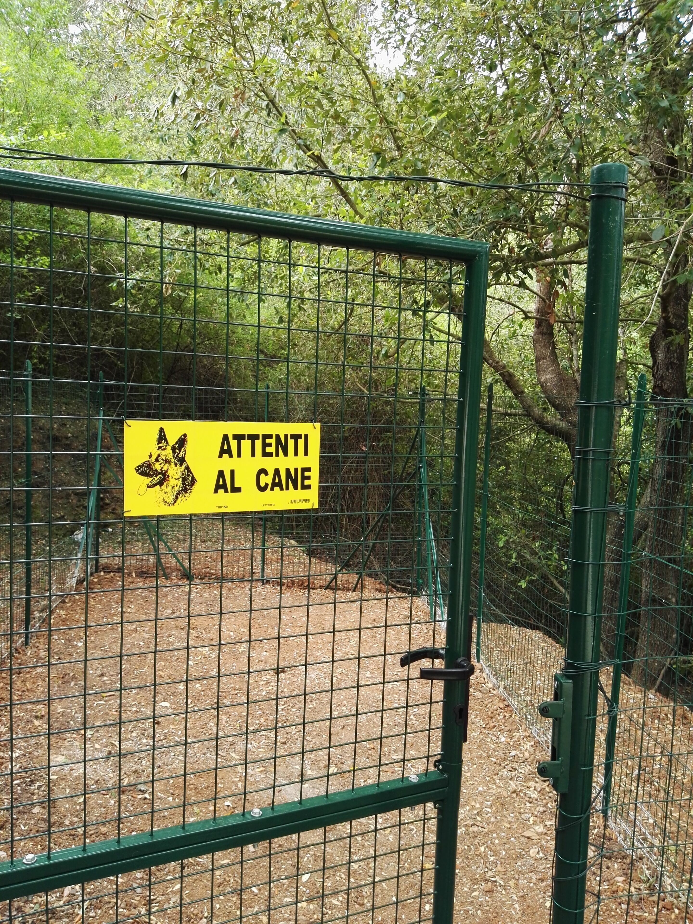Ein gelbes Schild mit schwarzem Text an einem grünen Metallzaun.
