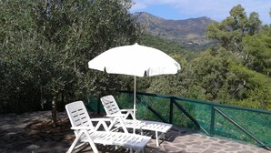 Un pati amb caires i un parasol blancs, amb vista a un paisatge de muntanyes.
