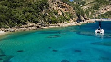 A coastal area with clear turquoise waters, rocky cliffs, and a boat anchored near the shore.