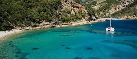 A coastal area with clear turquoise waters, rocky cliffs, and a boat anchored near the shore.