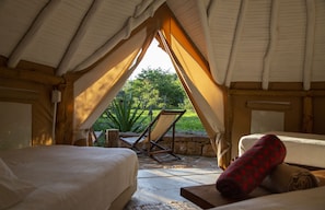 Un hébergement confortable en forme de tente, comprenant deux lits, une chaise et une vue sur la verdure environnante.
