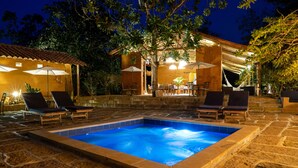 A swimming pool with lounge chairs and umbrellas, surrounded by stone walls and trees. - Nativo Glamping (Barichara)