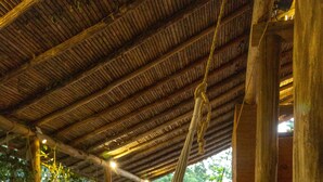 A hammock under a wooden roof, a brick floor, and a view of greenery outside. - Nativo Glamping (Barichara)
