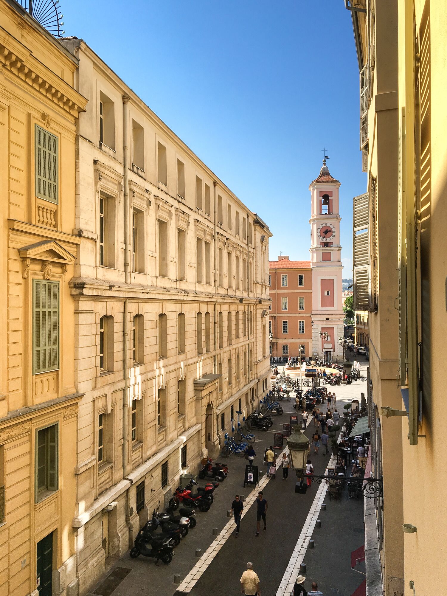 A street view with historic buildings, a clock tower, and a busy pedestrian area.