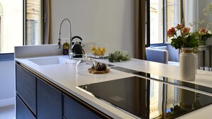 A modern kitchen with a large island, a built-in oven, and a sink. There is a vase with flowers on the island, and a kettle on the countertop. - Spacious 3BR / 3BA Apartment in Old Town Nice • 2-Min Walk to Beach • Full A/C (Nice)