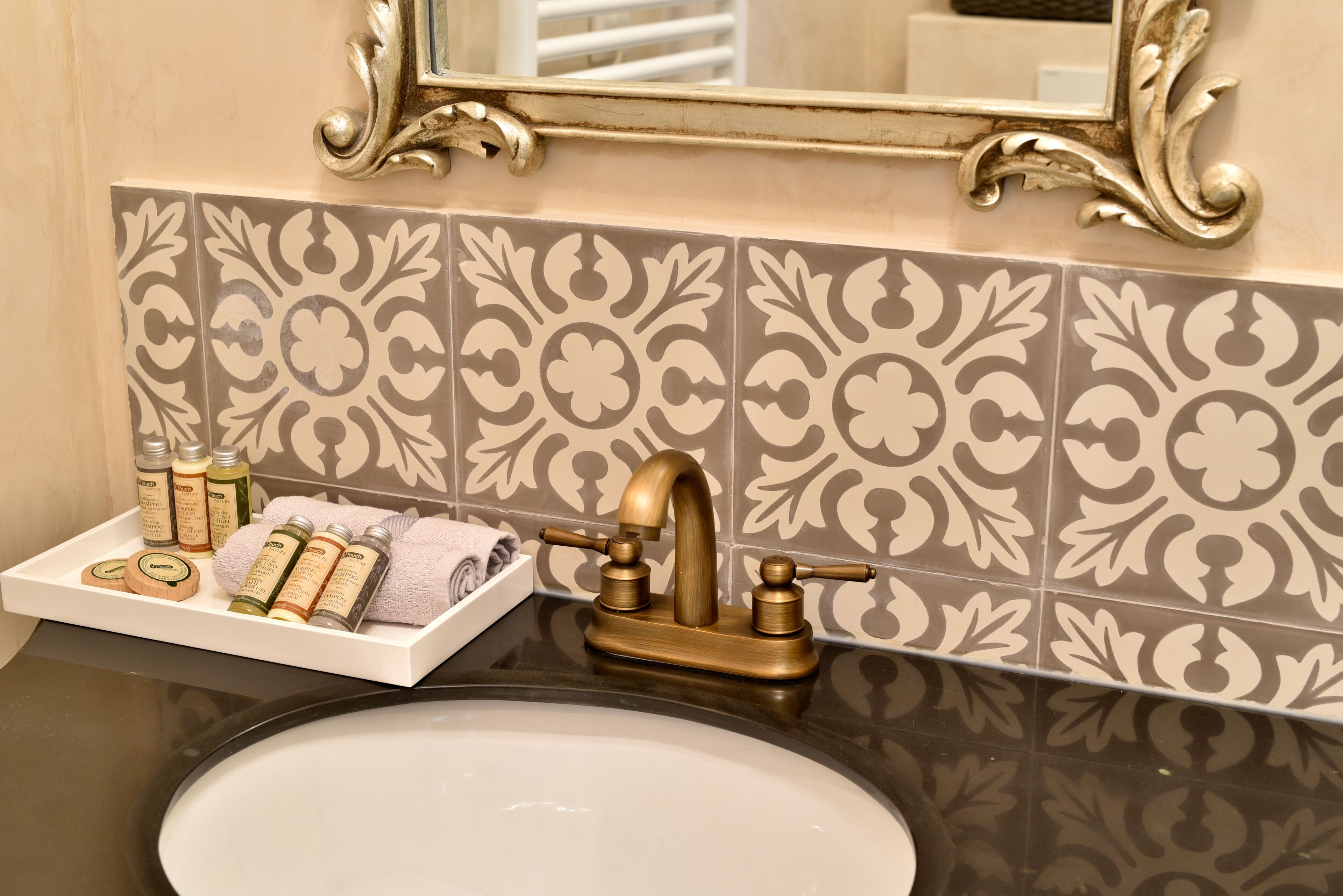 A bathroom with a gold faucet, a white sink, and a tray with toiletries.