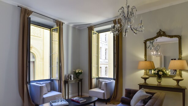 A modern living room with a sofa, armchair, and coffee table. There is a chandelier, a mirror, and a window with curtains. - Spacious 3BR / 3BA Apartment in Old Town Nice • 2-Min Walk to Beach • Full A/C (Nice)