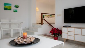 Una sala de estar moderna con comedor, una escalera y un televisor en la pared.