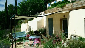 A patio with a table and chairs, a wooden fence, and a building with a door and window. -  COUNTRYSIDE AIR-CONDITIONED COTTAGE, PRIVATE POOL  NEAR BANDOL SANARY CASSIS (Évenos)