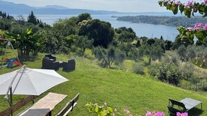 A picnic setup with a table and benches, surrounded by lush greenery and a view of a lake and distant mountains. - Your country Villa with a amazing view, private garden and private pool! (salò (bs))