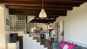 A spacious living area with a grey sofa, a television, and a staircase leading to a kitchen. - Your country Villa with a amazing view, private garden and private pool! (salò (bs))