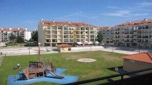 A playground with a slide and climbing structures, surrounded by a grassy area and a sports field.