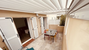 Une terrasse couverte avec une table et des chaises, une plante en pot et une porte coulissante.