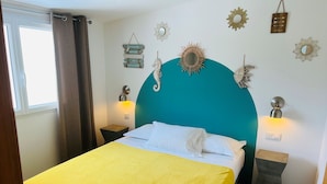 Un lit avec une couvre-lit jaune, une tête de lit turquoise et des oreillers blancs. De chaque côté du lit, on trouve des lampes fixées au mur.