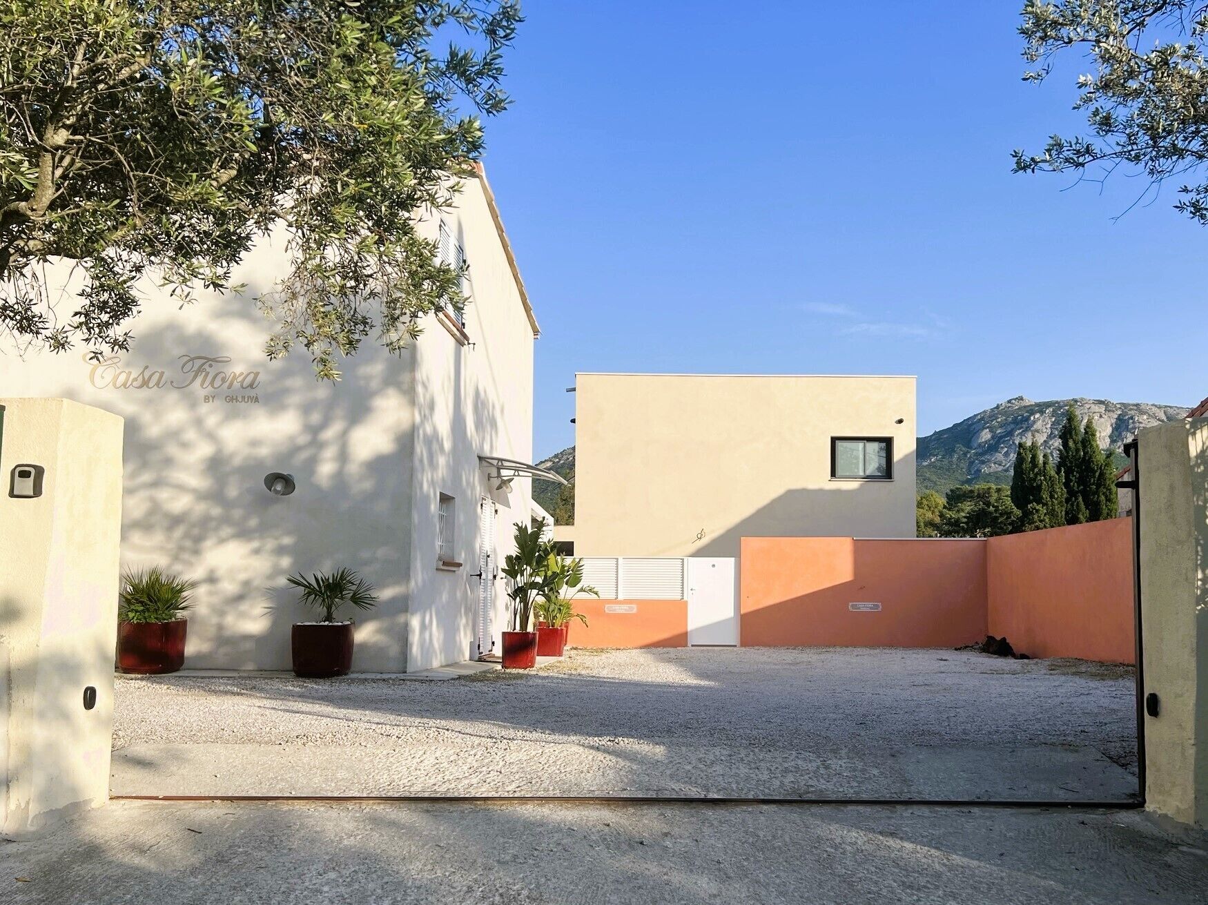 A building with a white facade and a beige section, surrounded by gravel and potted plants.