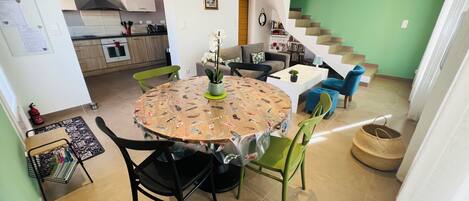 A dining area with a round table covered by a tablecloth with fish patterns, surrounded by green chairs.