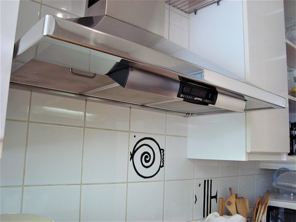 Una cocina con armarios blancos, una campana extractora de acero inoxidable y un salpicadero de azulejos con un diseño espiral negro.