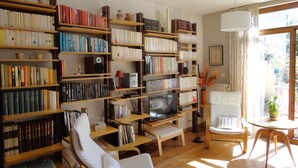 Ein gemütliches Wohnzimmer mit Holzbücherregalen, die mit Büchern gefüllt sind, einem Fernseher und bequemen Sitzgelegenheiten.