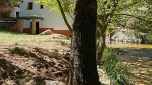 A white building with a red base, a tree in the foreground, and a clear stream in the background. - Rural house Nº13 Molino Jaraiz for 8 people (Yeste)