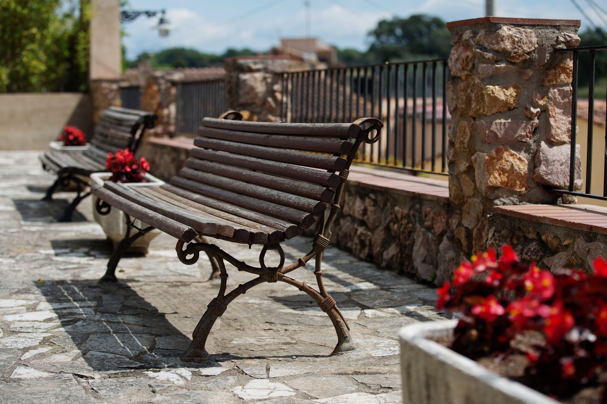 A stone bench with metal armrests and a stone wall behind it.