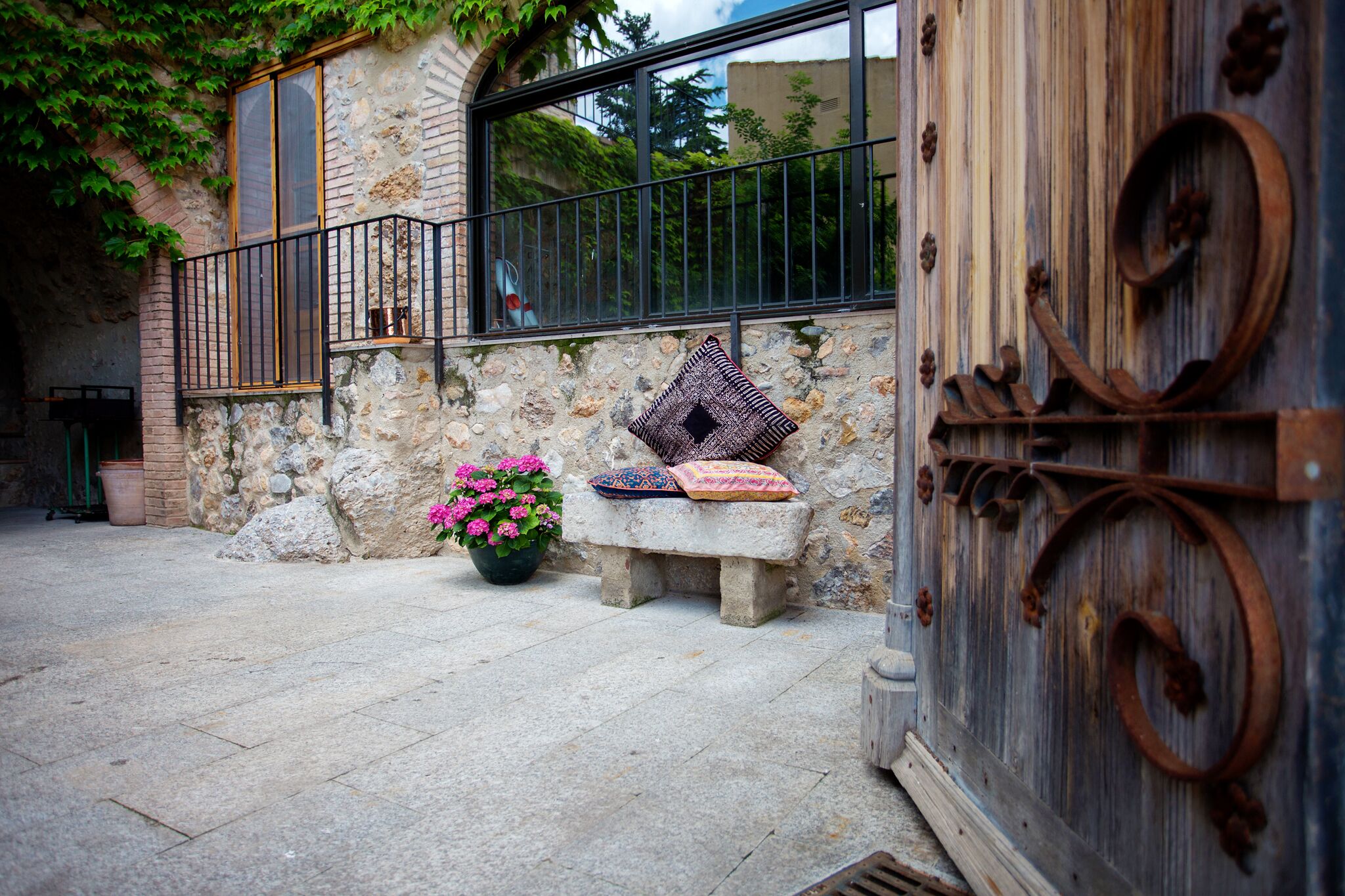 A stone building with a bench, a potted plant, and a decorative metal gate.