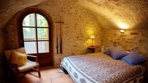 A rustic room with a stone wall, a wooden chair, a bed with a floral bedspread, and a lamp on a small table. - 800 Square Meter Unique Property On Costa Brava (Sant Mori)