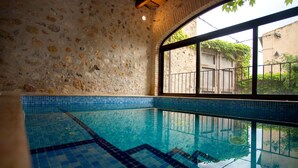 An indoor swimming pool with stone walls and a view of a building through a large window. - 800 Square Meter Unique Property On Costa Brava (Sant Mori)