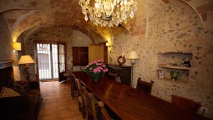 A dining area with a long wooden table, chairs, and a chandelier. There is a fireplace with a stone wall and a wooden door in the background. - 800 Square Meter Unique Property On Costa Brava (Sant Mori)
