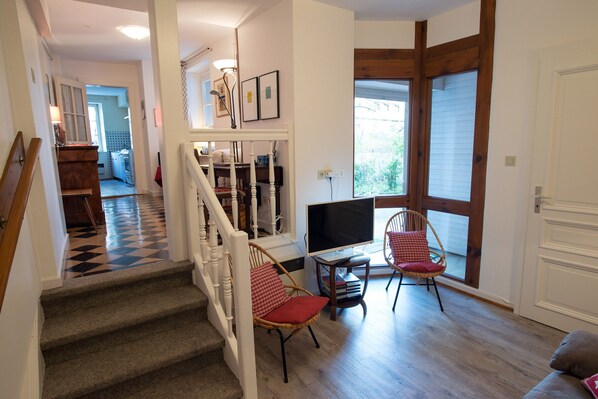 A staircase leading to a living area with a TV, two wicker chairs, and a bookshelf.