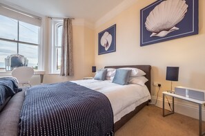 Habitación de hotel con una cama grande, un escritorio, una silla y dos obras de arte enmarcadas en la pared.