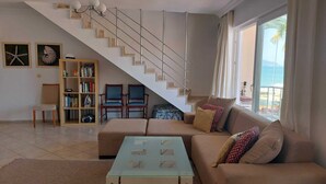 A living room with a staircase, a sofa set, a coffee table, a bookshelf, and a view of the sea. - Poseidon 3, seafront 3 bedroom apartment with unobstructed beach and sea views. (Calis Plaji)