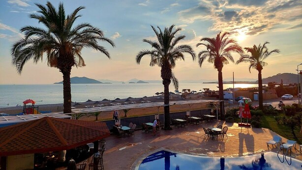 A poolside area with a view of the sea, palm trees, and beach umbrellas. - Poseidon 3, seafront 3 bedroom apartment with unobstructed beach and sea views. (Calis Plaji)