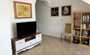 A living room with a TV, a bookshelf, and two framed pictures on the wall. - Poseidon 3, seafront 3 bedroom apartment with unobstructed beach and sea views. (Calis Plaji)