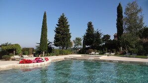 Ein klares Schwimmbecken mit Liegestühlen und ein gepflegter Garten mit hohen Bäumen und Sträuchern.