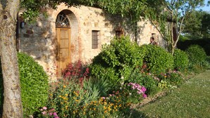 Ein rustikales Steinhaus mit Holztür und -fenstern, umgeben von einem üppigen Garten mit verschiedenen blühenden Pflanzen.
