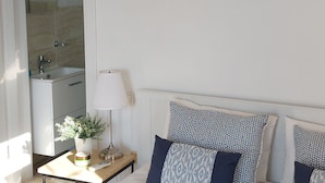 Une chambre à coucher avec un lit, une table de chevet avec une lampe, une plante en pot et des coussins à motifs.